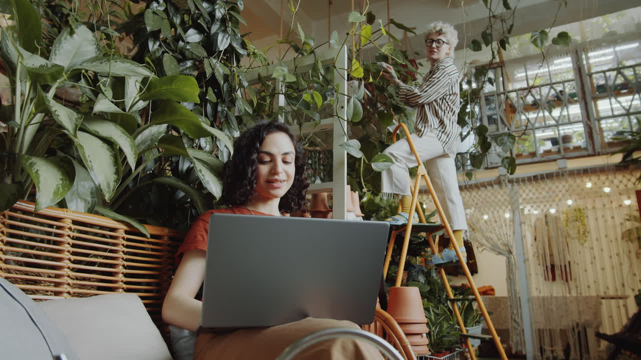 chica trabajando en una computadora portátil en una tienda de flores y hablando con un colega