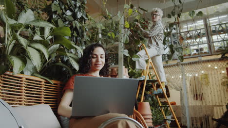 girl working on laptop in flower shop and talking with colleague