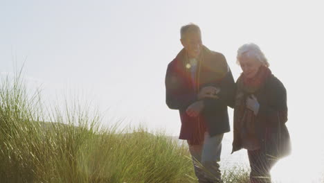 loving active senior couple hugging as they walk along coastal path against flaring sun