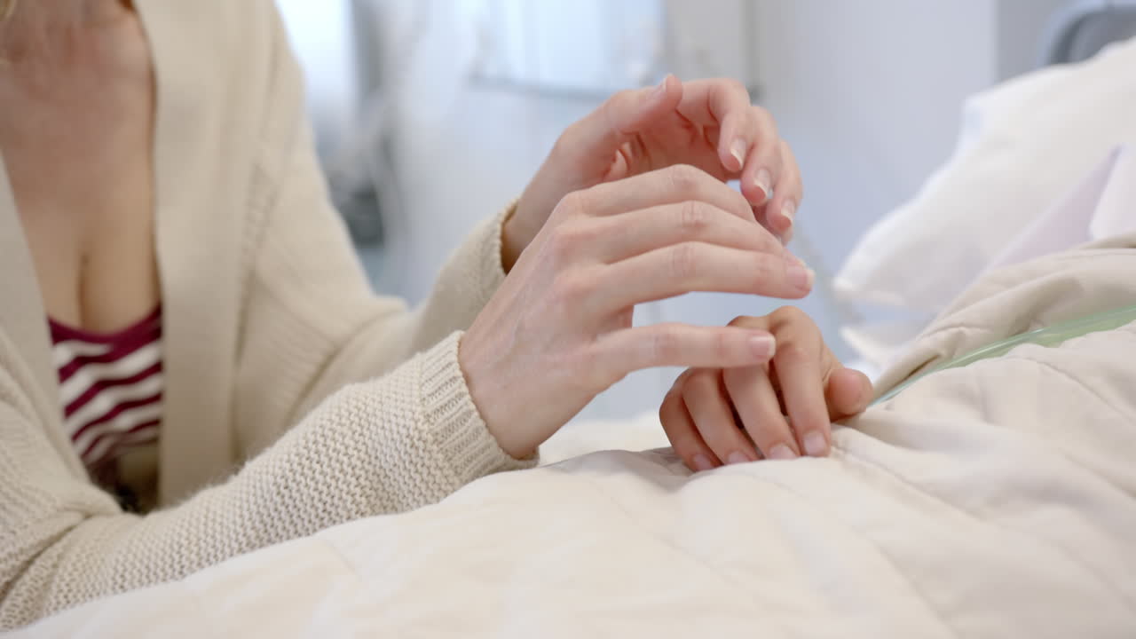 病院のベッドに横たわる娘の患者の手を握る白人母親、スローモーション