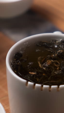 pouring hot water over tea leaves in a white cup