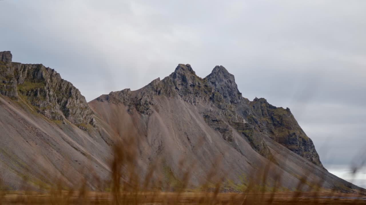A breathtaking view of the towering, rugged peaks and eroded slopes of Vestrahorn mountain, dominating the vast landscape of Stokksnes, Iceland, under a soft, overcast sky