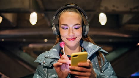 woman listening music walking at night closeup. girl headphones holding lollipop