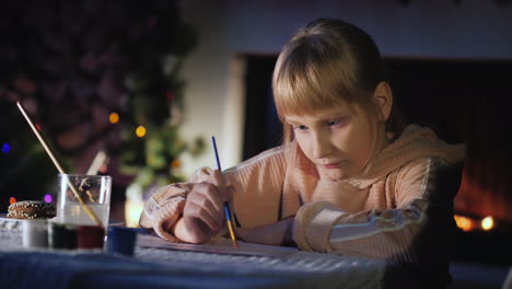 niño escribe una carta a santa claus cerca de la chimenea y el árbol de navidad