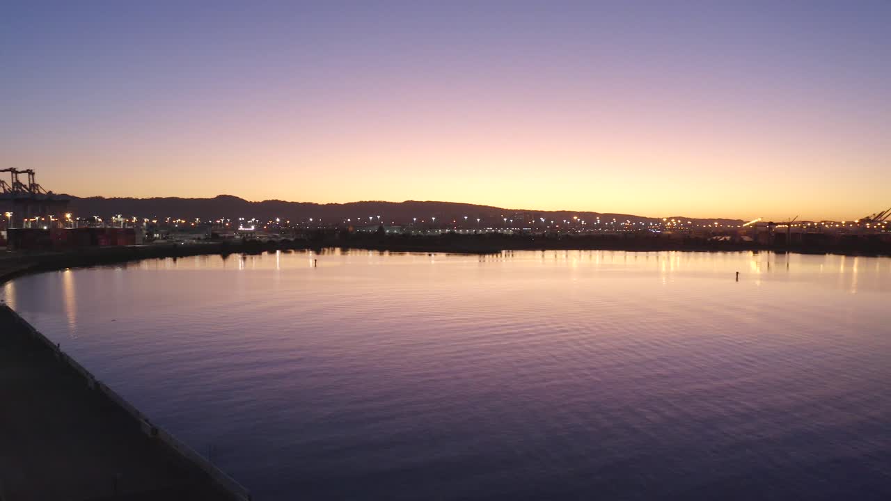 산을 배경으로 하는 넓은 지역 운송 항구와 보라색 만 위로 눈부시게 피는 일출