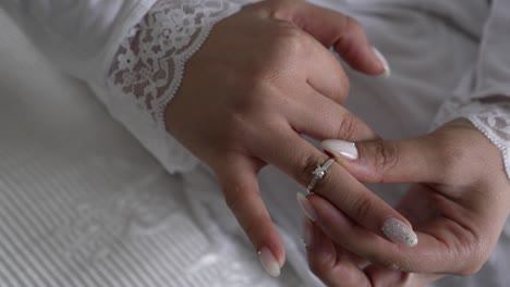 a bride in her wedding dress places her engagement ring on her finger