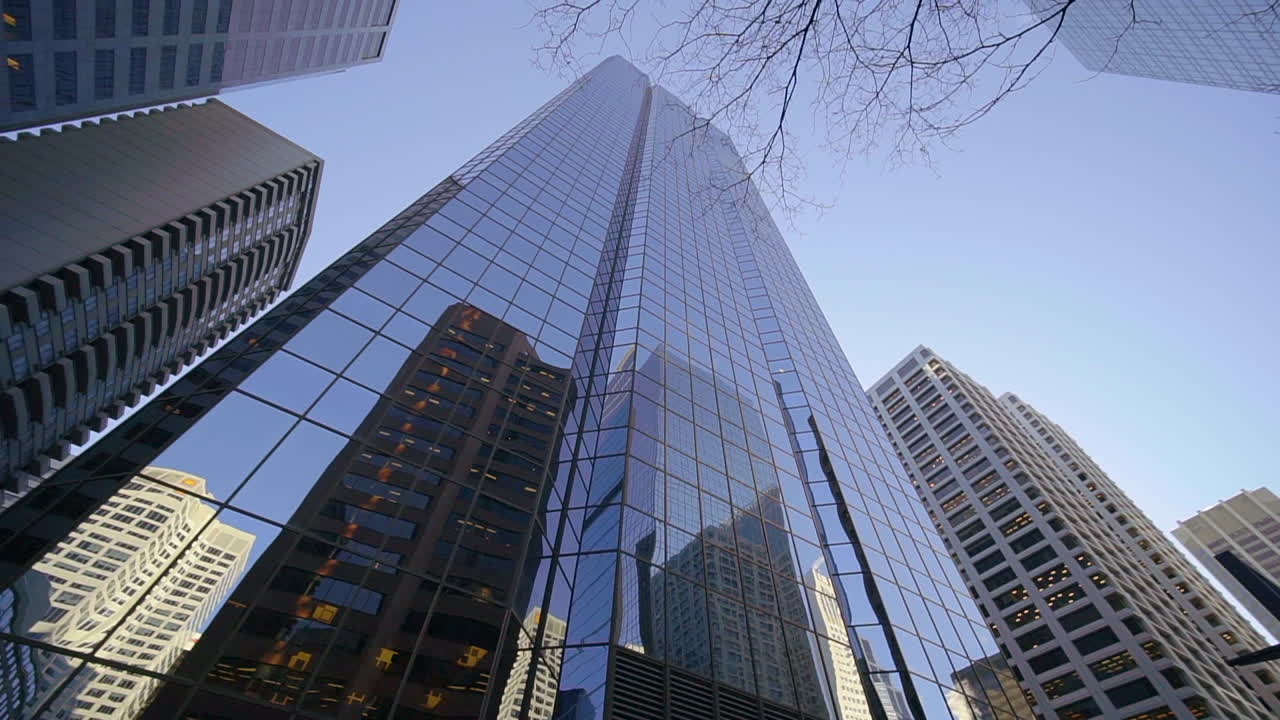 Looking up at skyscrapers in downtown Calgary, Canada while rotating. Daytime shot with sunny, bright blue sky. Other buildings are reflected in the windows. Slow motion.