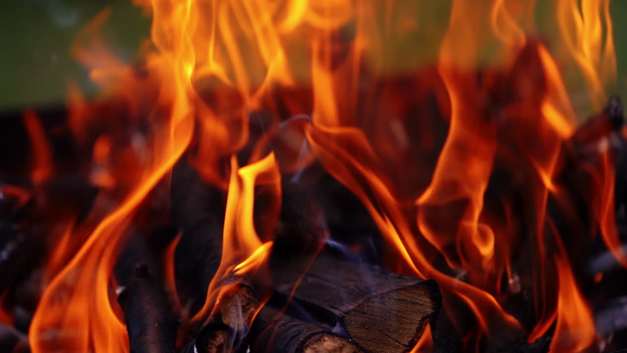 Wood in fire for barbeque. Red flame burning brightly on the black logs outdoors. Background of fire. Close-up. Slow motion.