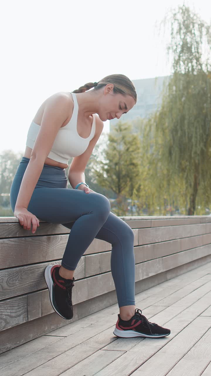 Mujer corredora atlética en ropa deportiva con dolor de rodilla después de hacer ejercicio en un parque urbano en un día soleado