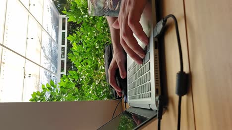 Vertical-shot-of-hands-scrolling-and-typing-on-a-laptop-while-on-a-summer-resort,-candid-moment-of-a-digital-nomad-lifestyle