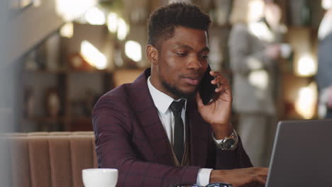 black businessman using laptop and talking on phone in restaurant