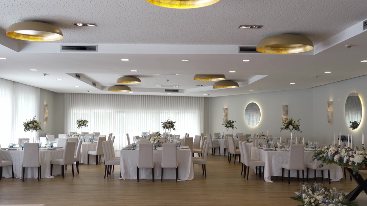 Amplio salón de bodas con elegantes montajes de mesa, centros de mesa florales e iluminación moderna.