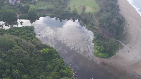 aguas tranquilas del río con el reflejo de las nubes cerca del complejo lalit en la playa de rajbagh, canacona, goa del sur, india - toma aérea de drones