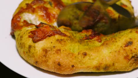freshly baked mozzarella and tomato pesto garlic bread being cut with rolling pizza cutter. fresh italian side dish food