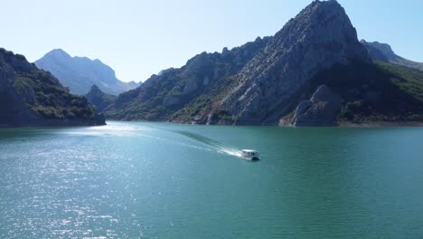 Clip-Cinematográfico-De-Drones-Sobre-Un-Lago-Exótico-Y-Un-Barco-Moviéndose-A-Través-Del-Agua-En-El-Lago-De-Riaño-En-Castilla-Y-León,-España