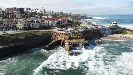 4K-Antenne-Einer-Drohne,-Die-Sich-Von-Der-Küste-Von-La-Jolla-Beach-In-Kalifornien-Zurückzieht,-Wobei-An-Einem-Sonnigen-Tag-Wellen-Auf-Die-Felsen-Spritzen