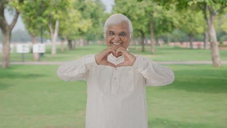 happy indian old man showing heart sign in park