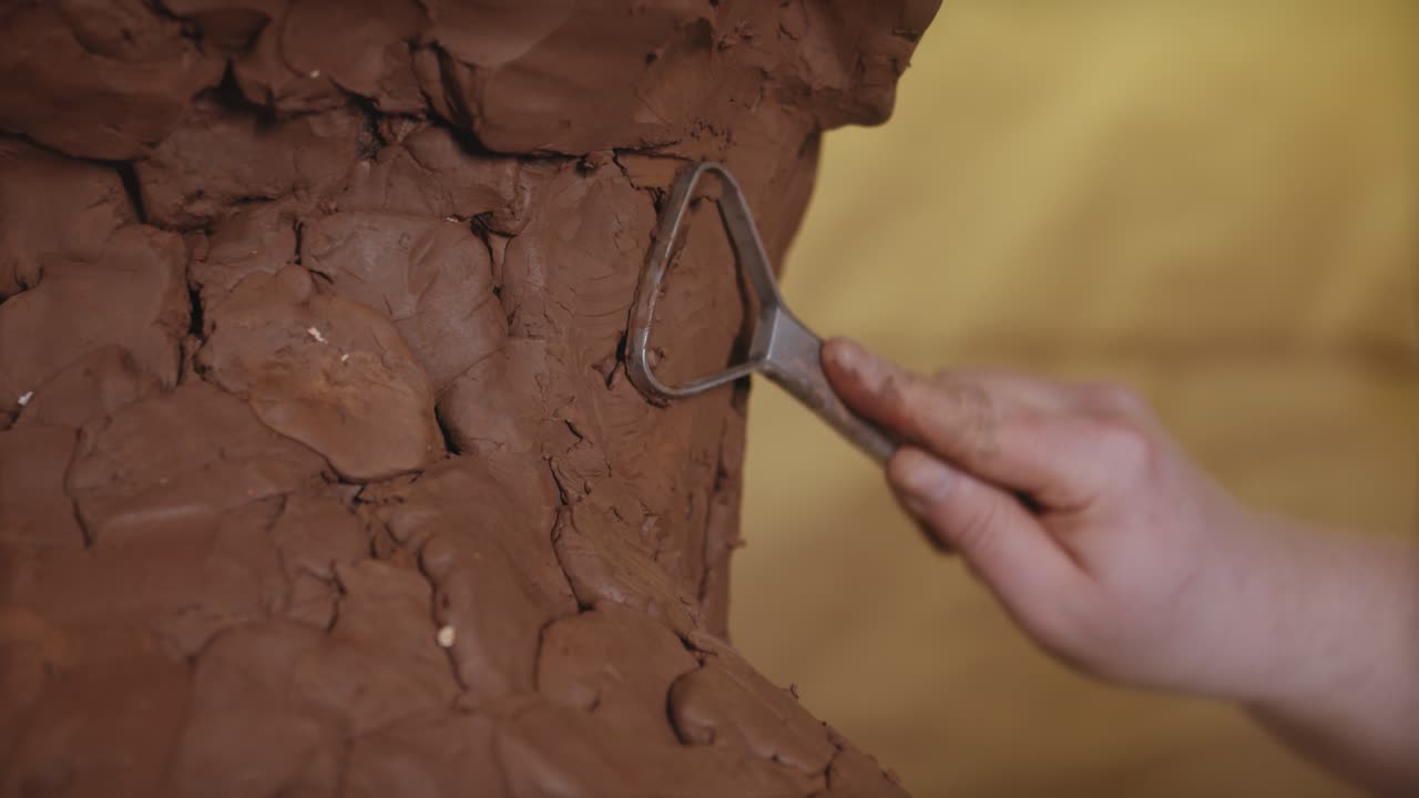 한 남자가 점토 조각을 조각하고 있으며, 그의 손은 재료를 능숙하게 형성하고 형성하고 있습니다.