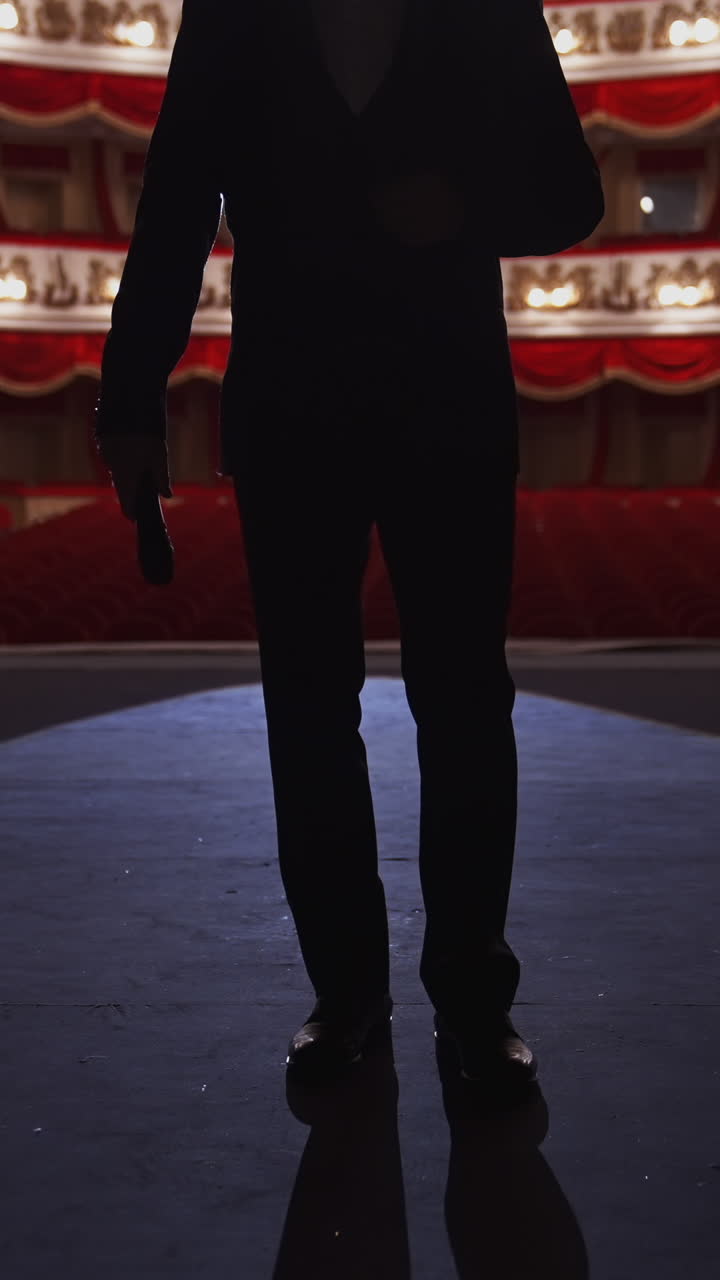 Man in suit standing on stage back to auditorium. Dark silhouette of unrecognizable actor on the background of classic theatre hall in red and white colors. Vertical video