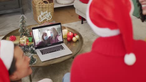 Eine-Vielfältige-Familie-Mit-Weihnachtsmützen-Nutzt-Laptop-Für-Einen-Weihnachtsvideoanruf-Mit-Der-Familie-Auf-Dem-Bildschirm