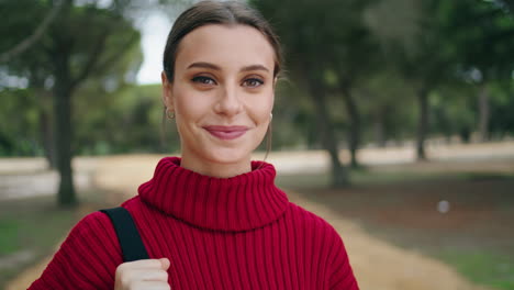 Vertical-portrait-young-woman-standing-in-green-forest-wearing-red-sweater.