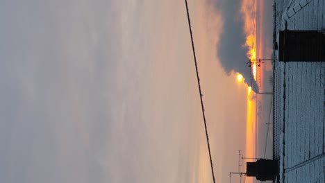 vertical clip: industry smoking chimney above frosty freezing home rooftops during orange glowing sunrise