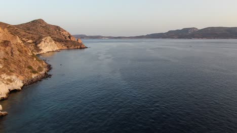 Drone view in Greece flying over blue sea next a brown hill mountain at sunset in Milos