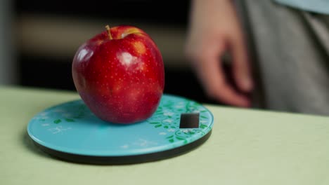 a man weighs a fresh red apple on a kitchen scale, close-up