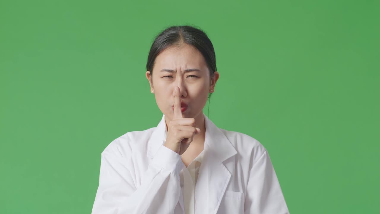 Woman in lab coat gesturing shhh