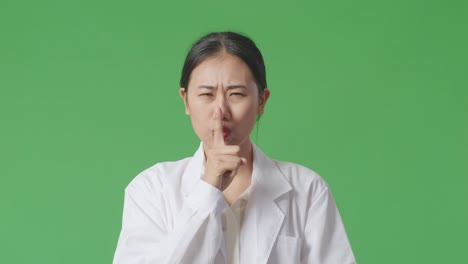 woman in lab coat gesturing shhh