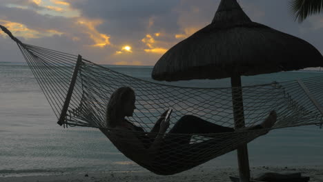 mujer con teléfono tendido en una hamaca en la playa