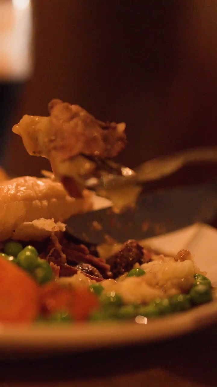 Una mano taglia un tortino di carne con verdure in un'atmosfera calda e soffusa di un ristorante.