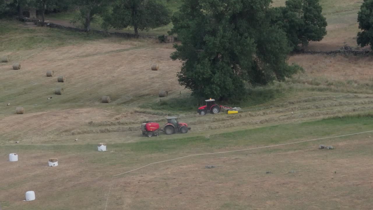 filmando drones de 167 mm y en cámara lenta algunos prados que están siendo cosechados por maquinaria agrícola, un tractor alinea el heno y otro hace alpacas con una embaladora, apreciamos cómo expulsa un