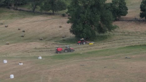 Filmando-Con-Drones-De-167-Mm-Y-En-Cámara-Lenta-Algunas-Praderas-Que-Están-Siendo-Cosechadas-Por-Maquinaria-Agrícola,-Un-Tractor-Alinea-El-Heno-Y-Otro-Hace-Alpacas-Con-Una-Empacadora,-Apreciamos-Como-Expulsa-Una