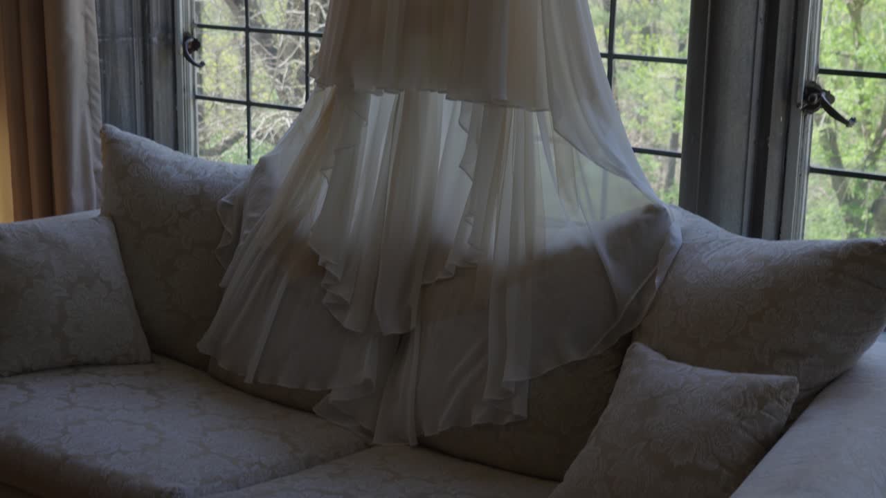 백색 웨딩 드레스가 맨어 하우스 납 창문 앞에 매달려 있으며,  ⁇ 을 내려다보고 있습니다.