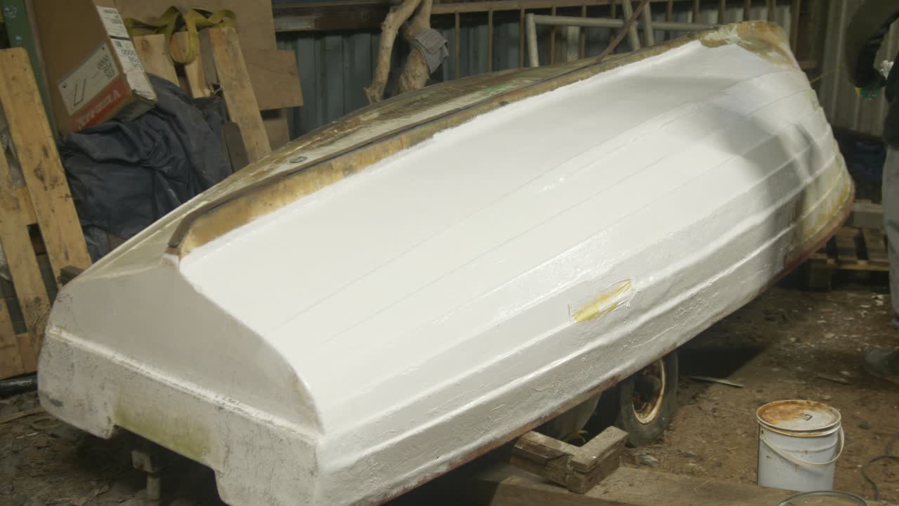 Rolling on white polyester topcoat to upturned fiberglass boat hull