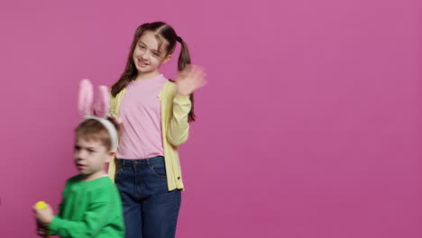 Cute-brother-and-sister-posing-against-pink-background-in-studio