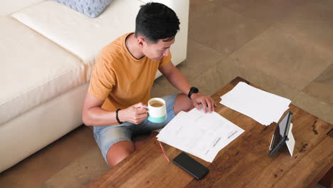 young man reviewing documents at home with tablet and coffee on table