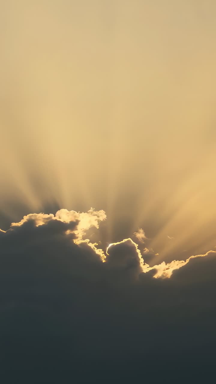 Vertical video: Shifting sun behind cloud bank creating bright rim, crepuscular rays at sunrise