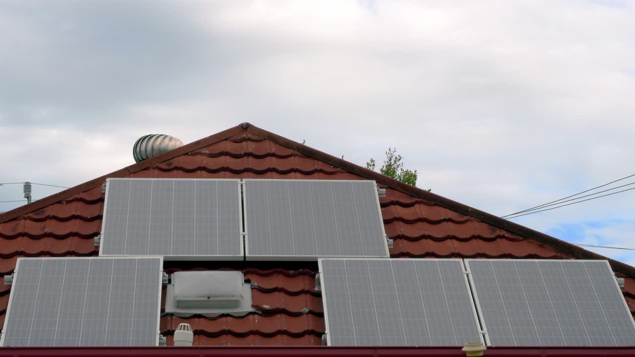 Time lapse, four solar panels on house roof, clouds pass in background, fixed medium shot