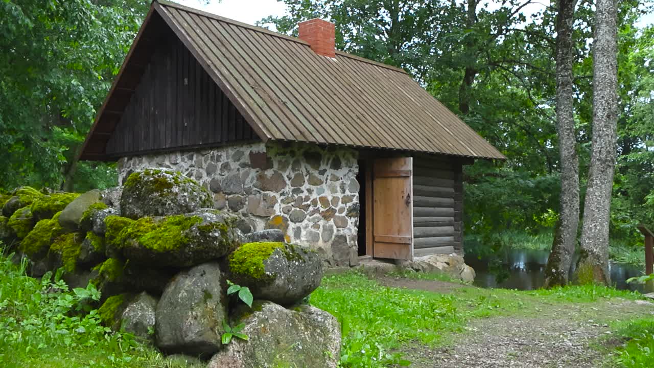 Old historic stone and wooden building sauna from a iconic movie called kevade. Surrounded with old mossy stone fence during a summer cloudy day with palamuse river in the background