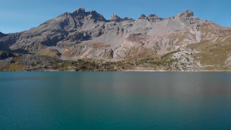 Aerial-flyover-the-islands-in-the-waters-of-Lac-de-Salanfe-in-Valais,-Switzerland-on-a-sunny-autumn-day-in-the-Swiss-Alps-with-a-view-of-surrounding-alpine-peaks-and-cliffs