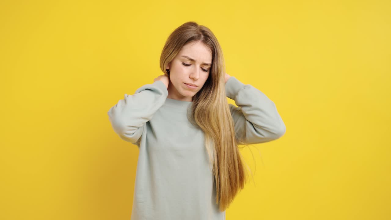 Young woman massaging neck on yellow background