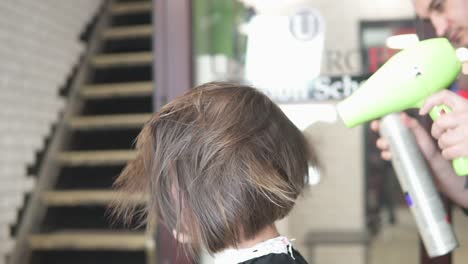 professional hairdresser using a hairdryer after haircut and applying hair treatment spray