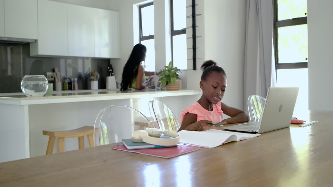 Mom at counter checking phone child drinking juice leaning to laptop studying at table, copy space