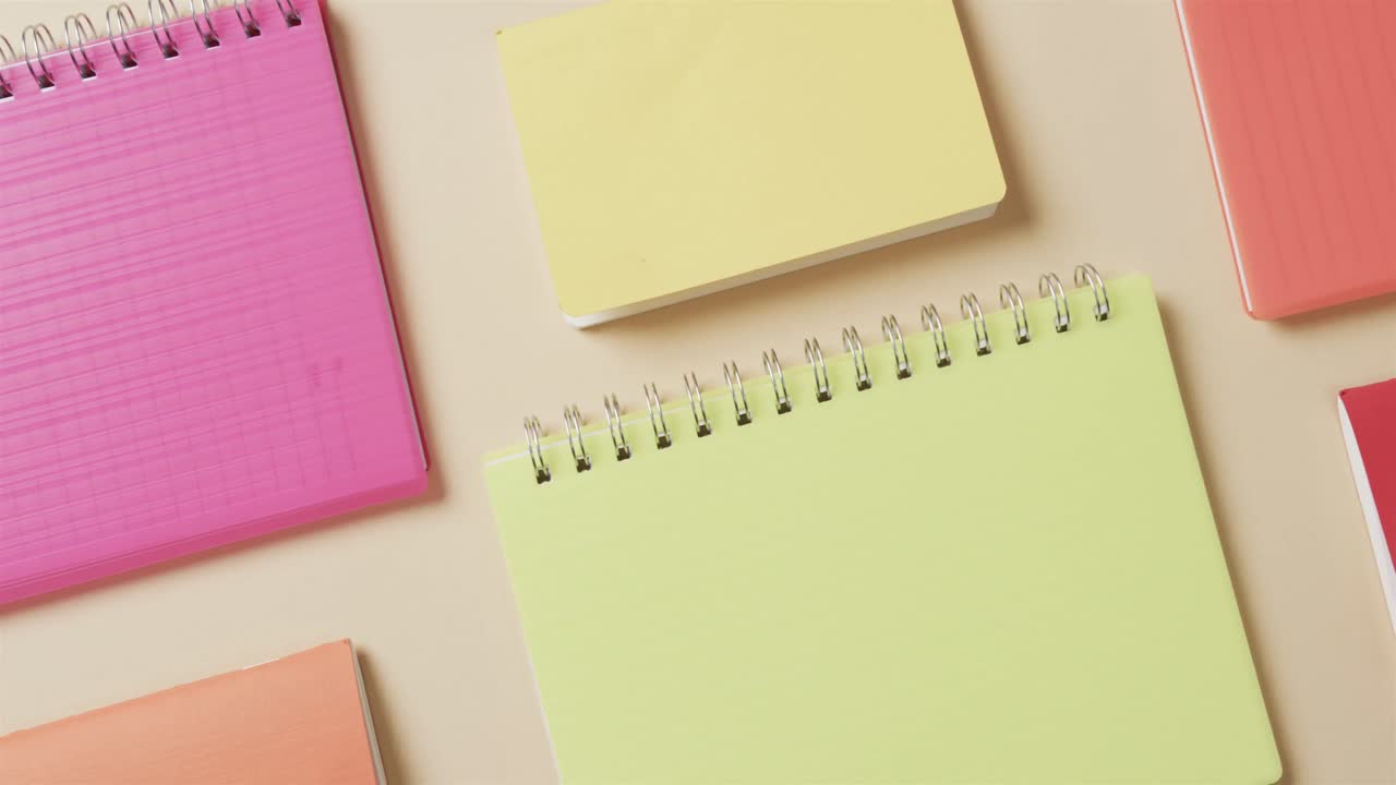 Overhead view of colourful notebooks arranged on beige background, in slow motion