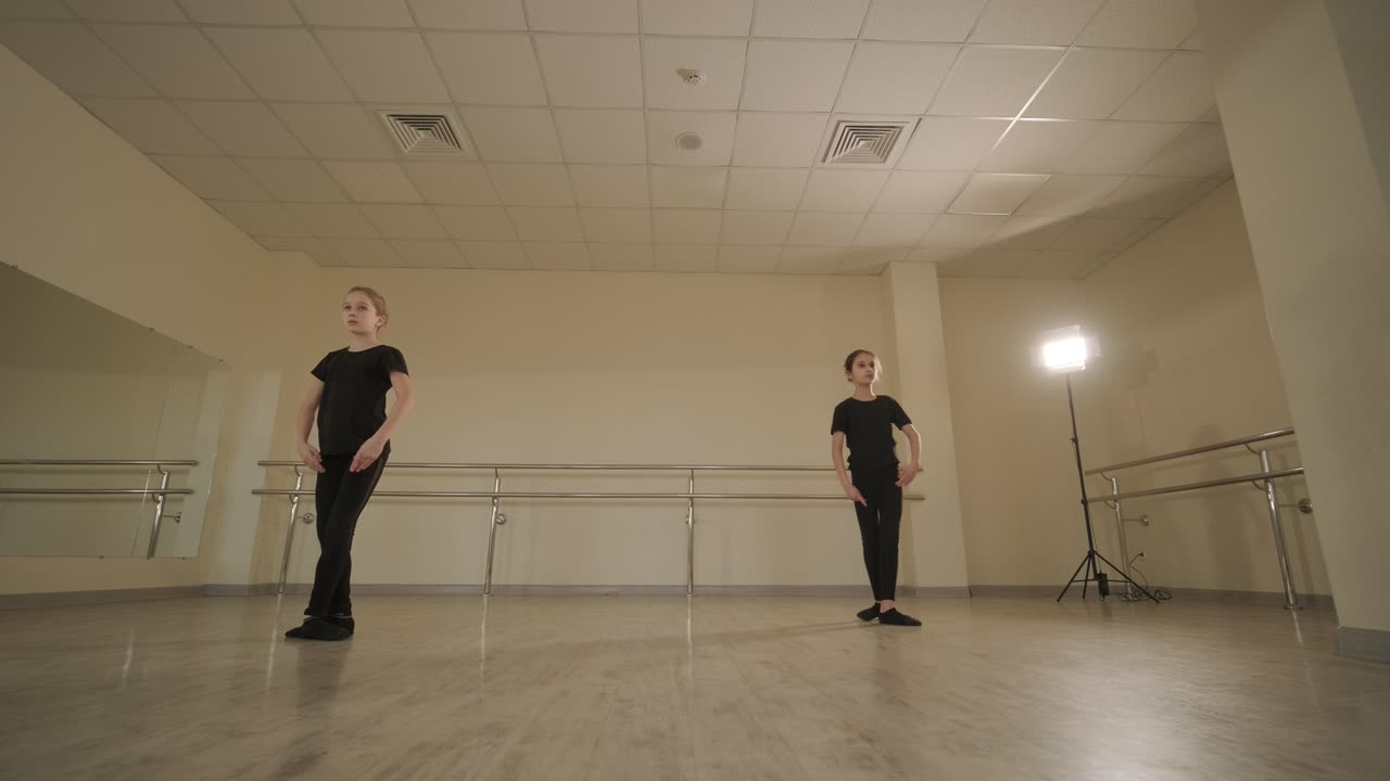 un grupo de jóvenes estudiantes de ballet con ropa de baile negra practicando posiciones en un amplio estudio de ballet con pisos de madera y barras montadas en la pared. expresiones enfocadas y movimientos sincronizados.