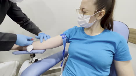 captura de una enfermera esterilizando y sintiendo el brazo de una mujer para encontrar una vena y luego haciendo la incisión con la aguja