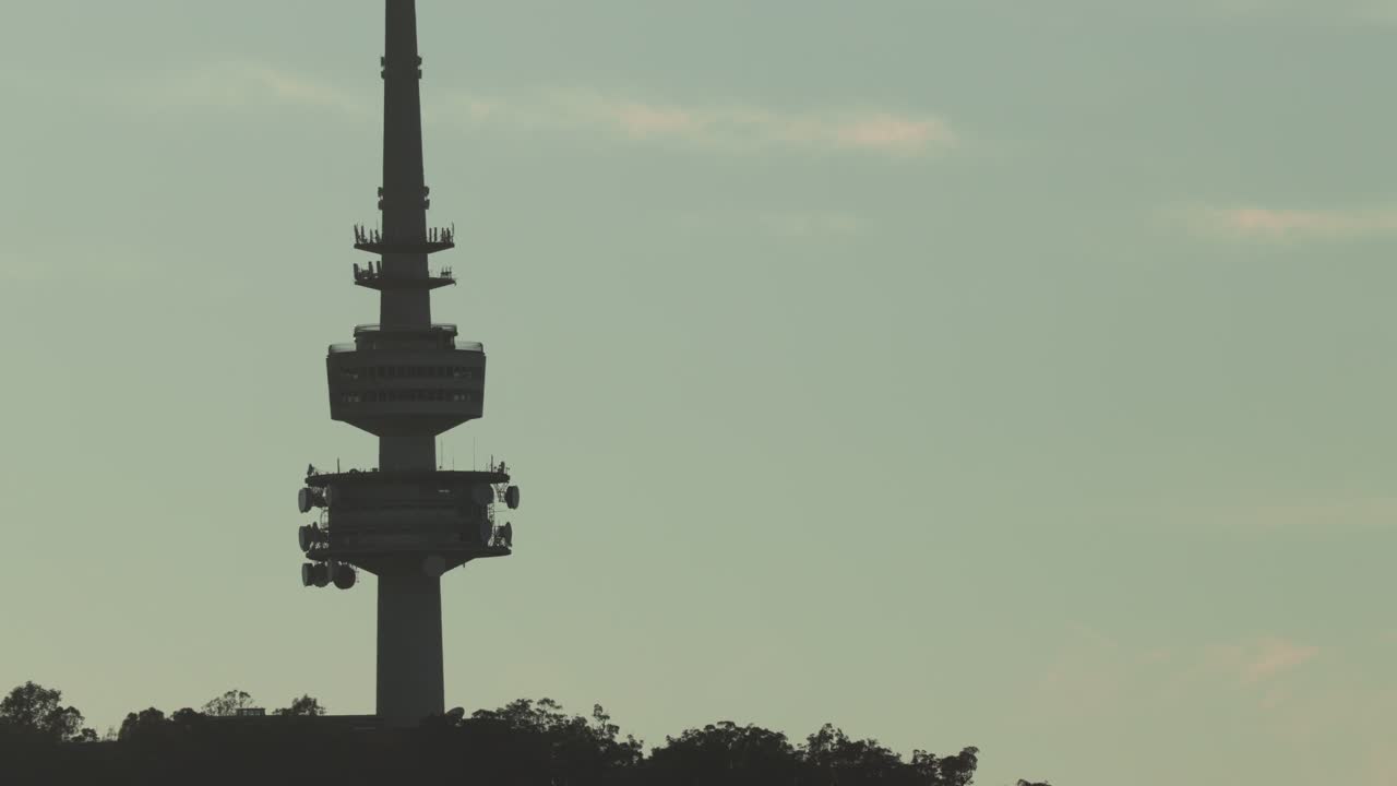 A gentle zoom out from the close view of Canberra Tower, silhouetted against a pastel blue sky at sunrise