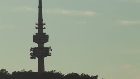 a gentle zoom out from the close view of canberra tower, silhouetted against a pastel blue sky at sunrise